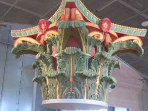 Bunter Säulenaufsatz mit floralen Motiven und Verzierungen in Grün, Rot und Gelb.