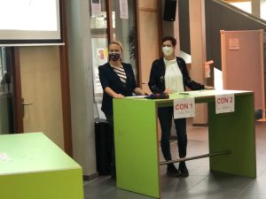 Zwei Personen stehen hinter einem Empfangstresen mit den Beschriftungen 