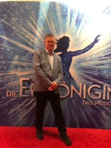 Eine Person steht auf einem roten Teppich vor einem Hintergrund mit dem Schriftzug 