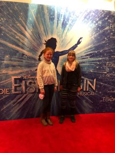Zwei Mädchen stehen auf einem roten Teppich vor einem Hintergrund mit dem Motiv des Musicals 