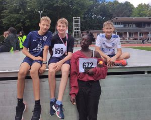 Vier Kinder stehen auf einer Plattform. Drei Jungen sitzen, einer trägt ein Fußballtrikot mit der Nummer 656, der andere ein Trikot mit der Aufschrift 