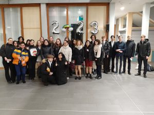 Eine Gruppe von etwa 30 Personen steht in einem Innenraum, umgeben von großen Luftballons mit der Zahl 