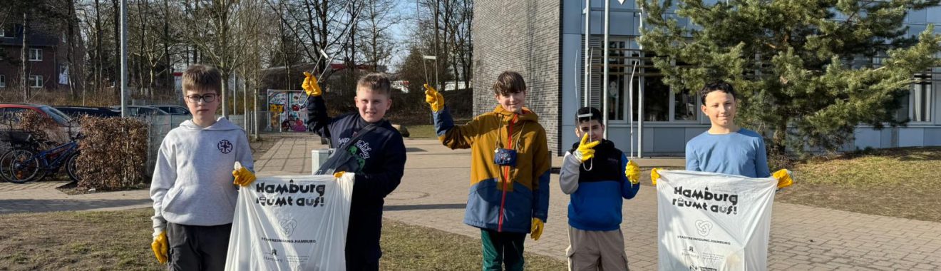 Fünf Kinder stehen auf einer Wiese vor einem Gebäude. Sie tragen gelbe Handschuhe und halten Müllsäcke in den Händen. Im Hintergrund sind Bäume und ein gepflasterter Weg zu sehen. Es ist ein sonniger Tag.