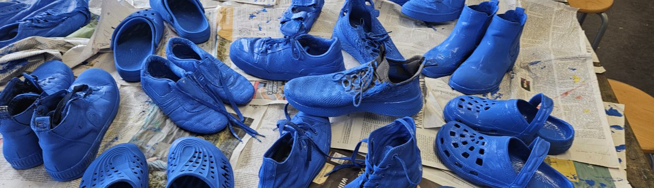 Eine Vielzahl von Schuhen in verschiedenen Formen und Stilen, die alle in leuchtendem Blau lackiert sind. Die Schuhe sind auf einer Tischoberfläche angeordnet, die mit Zeitungen bedeckt ist.