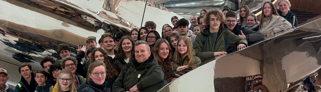 Gruppe von Menschen, die lächelnd in einem modernen, reflektierenden Raum posiert. Im Hintergrund sind gewundene, metallische Strukturen sichtbar.
