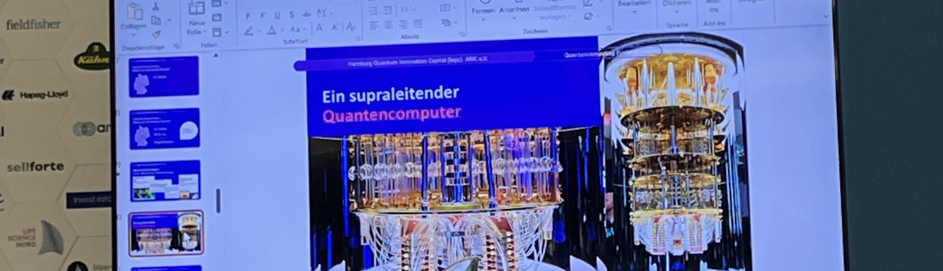 Ein Bildschirm zeigt eine Präsentation mit dem Titel "Der superschlanke Essensspender". Im Hintergrund sind verschiedene Folien zu sehen. Im Vordergrund stehen ein Wasserkaraffe und eine Snackschale auf einem Tisch, umgeben von einem hellen Tischdecken.