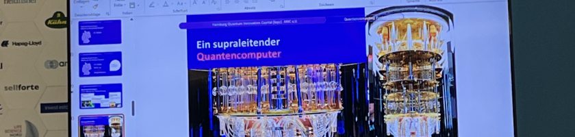 Ein Bildschirm zeigt eine Präsentation mit dem Titel "Der superschlanke Essensspender". Im Hintergrund sind verschiedene Folien zu sehen. Im Vordergrund stehen ein Wasserkaraffe und eine Snackschale auf einem Tisch, umgeben von einem hellen Tischdecken.