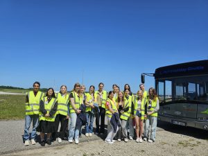 Gruppe von Personen in gelben Sicherheitswesten steht auf einem offenen Gelände neben einem Bus. Der Himmel ist klar und blau.